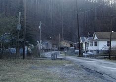 an empty street in the middle of a wooded area with houses and trees on both sides