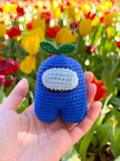 a hand holding a small crocheted toy in front of flowers