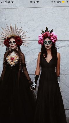 two women in black dresses with flowers on their heads, one wearing a skeleton mask