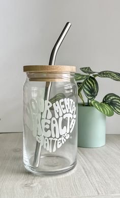 a glass jar with a metal straw in it and a potted plant next to it