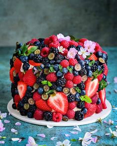 a cake with berries, strawberries and blueberries on top is surrounded by flowers