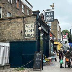 people are walking down the sidewalk in front of an ale cider meat