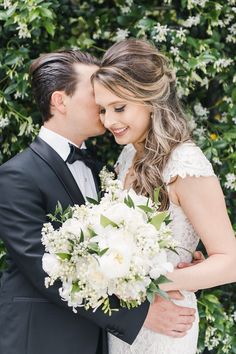 a bride and groom kissing in front of a bush with white flowers at their wedding