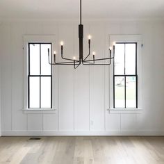 an empty room with three windows and a chandelier hanging from the ceiling,