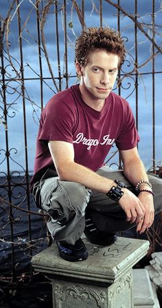 a young man sitting on top of a cement bench next to a metal fence and looking at the camera