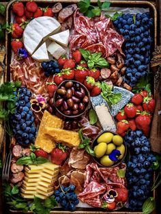 a tray filled with assorted fruits and meats next to cheese, grapes, strawberries