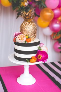 a black and white striped cake with a pineapple on top, surrounded by balloons