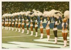 a group of cheerleaders standing on top of a field with pom poms