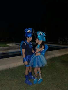 two children dressed up in costumes standing next to each other on the grass at night