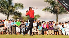 a man swinging a golf club in front of a large group of people on the grass