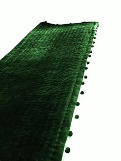 a green rug with pom - poms on the bottom is shown in front of a white background