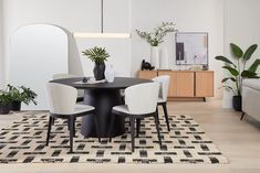 a dining room table with white chairs and a black round table surrounded by potted plants