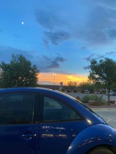 a blue car parked in a parking lot next to a street with the sun setting