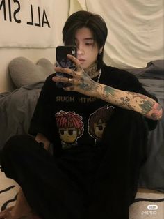 a person sitting on a bed taking a selfie with their cell phone and tattoos