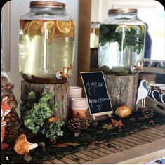 three jars filled with liquid and plants on top of a wooden table next to a chalkboard