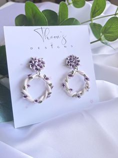 a pair of earrings with flowers on them sitting next to a card and some greenery