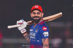 a man holding a cricket bat and wearing a red hat with his hand on the back of his shoulder