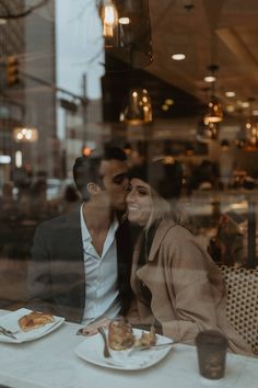 a man and woman sitting at a table in front of a window with food on it