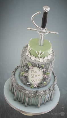 a three tiered cake decorated with flowers and a metal hook on top of it