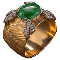 This 1950s-era band ring has been crafted by a master goldsmith. As with a fine Buccelatti jewel, every millimeter has been worked: from the freehand Florentine Finish to the gorgeously rendered four leaves -each set with 3 small white diamonds— and rendered in white gold. The jadeite stone measures 9.71 x 7.79mm and is a rich emerald green mottled with wisps of white clouds. The proportions on this ring are so balanced and authoritative; the jeweler who created this obviously created many, many Vintage Wide Band Jewelry For Formal Occasions, Vintage Wide Band Yellow Gold Jewelry, Antique Wide Band Jewelry For Formal Occasions, Formal Wide Band Gemstone Ring, Wide Band Gemstone Rings For Formal Occasions, Formal Heirloom Emerald Ring With Single Cut Diamonds, Vintage Hallmarked Wide Band Ring, Vintage Emerald Diamond Ring With Hallmark, Vintage Wide Band Hallmarked Rings