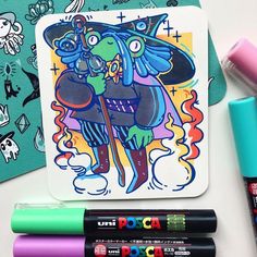 some markers and pens are sitting on a table next to an art card with a cartoon character