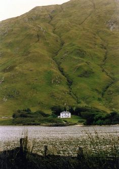 a white house sitting on top of a lush green hillside next to a body of water