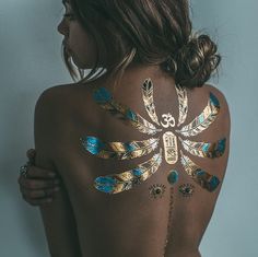 the back of a woman's body with gold and blue feathers painted on it