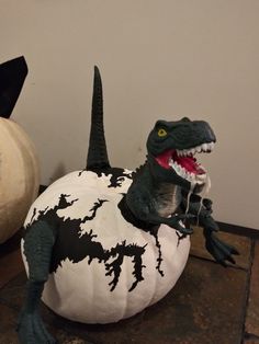 a fake dinosaur sitting on top of a white pumpkin next to a black and white pumpkin