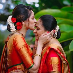 two women in red and orange saris are kissing each other with their heads together