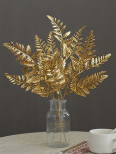 a vase filled with golden leaves on top of a table next to a white cup