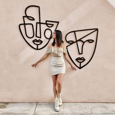 a woman standing in front of a wall with two masks on it