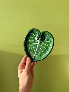 a person holding a green heart shaped plate in front of a green wall with the shape of a leaf on it