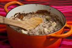 an orange pot filled with oatmeal sitting on top of a pink and red table cloth