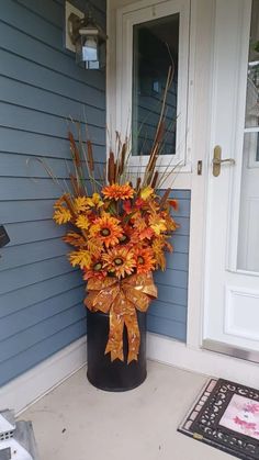 a large vase filled with lots of flowers on the front door step next to a blue house