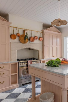 a kitchen with pink cabinets and marble counter tops, an island in the middle is surrounded by hanging utensils