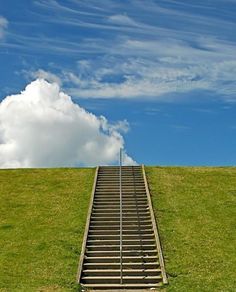 a stairway leading to the top of a grassy hill under a blue sky with clouds