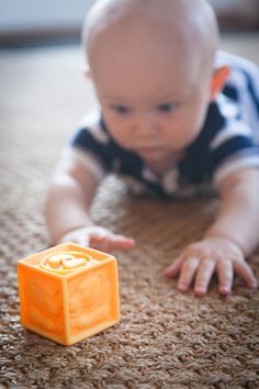 a baby laying on the floor next to an orange object that looks like a cube