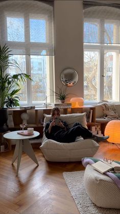 a person laying on a couch in a living room next to two windows and a lamp