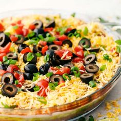 a dish filled with rice, black olives and green peppers next to some tortilla chips