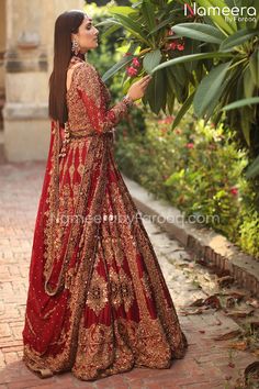 a woman in a red and gold bridal gown standing on a brick walkway next to flowers