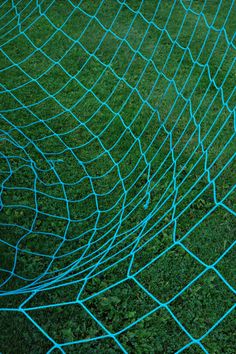 a soccer ball sitting in the middle of a blue net with grass behind it and a yellow frisbee on the ground