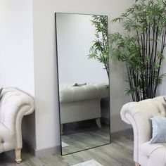 a large mirror sitting next to a white couch in a living room under a potted plant