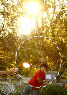 two boys are playing with a metal ring in the grass near flowers and trees as the sun shines behind them