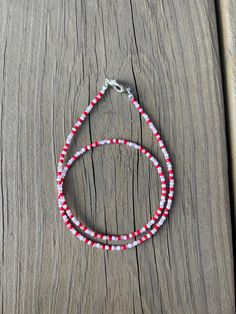 two red and white beaded bracelets sitting on top of a piece of wood