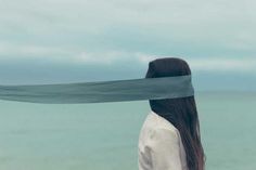 a woman standing on the beach with her long hair tied back