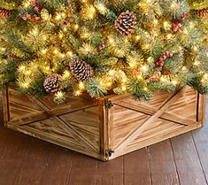 a christmas tree with pine cones and lights in a wooden crate on a wood floor