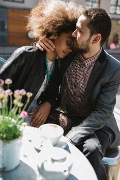 a man and woman sitting next to each other at a table with flowers in front of them