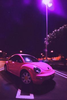 a pink car is parked on the side of the road at night with street lights in the background