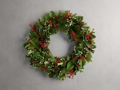 a christmas wreath with red berries and green leaves hanging on the wall next to a gray wall