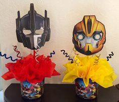 two vases filled with flowers and masks on top of a table in front of a wall